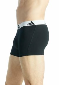 Slip neri realizzati in tessuto elasticizzato, con una fascia in vita bianca decorata da strisce nere con logo. Texture liscia e design aderente.