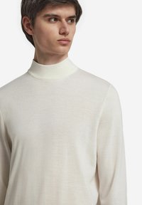 Ljust beige polokrage tröja tillverkad av mjukt, fint stickat material; åtsittande design med långa ärmar och minimal textur.