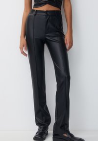 Pantalon noir en simili cuir à coupe slim, avec une taille plate, une fermeture à bouton et des coutures discrètes le long des hanches pour structurer.