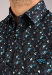 Maglietta nera a maniche corte con un motivo floreale astratto in turchese e bianco; presenta un piccolo logo blu e bottoni neri.