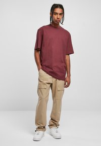 Bordo oversized majica, bež cargo hlače s bočnim džepovima i bijele tenisice. Casual outfit s opuštenim dizajnom.