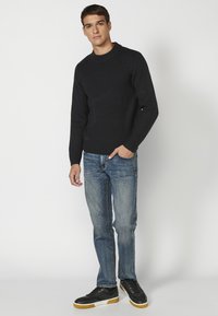 Marineblauer Strickpullover mit Rundhalsausschnitt, kombiniert mit hellblauen Denim-Jeans und schwarzen Sneakers mit Gummisohle.