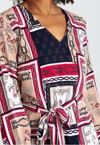 Blumig gemustertes Kleid in Marineblau, Pink und Weiß mit V-Ausschnitt, langen Ärmeln und gebundener Taille für eine figurbetonte Passform. Glatte Stofftextur.