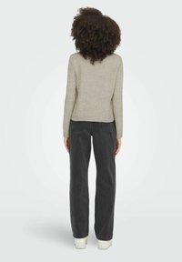 Lichtgrijze gebreide trui met een aansluitend ontwerp, geribde zoom en lange mouwen, gedragen met zwarte wijde jeans en witte sneakers.