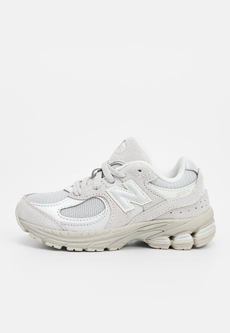 Zapatilla deportiva gris claro con materiales de malla y ante, forma redondeada, detalles en tonalidades similares y una entresuela texturizada con características de amortiguación.