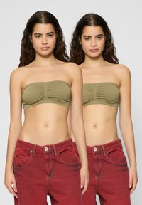 Olivovo zelený bandeau top s nariasenými detailmi, kombinovaný s vysokými červenými denimovými džínami s prednými vreckami a zapínaním na gombík.