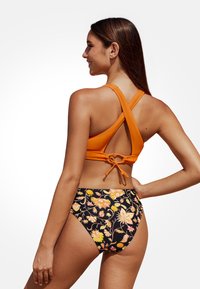 Badeanzug mit einem orangefarbenen, gekreuzten Oberteil und einem hoch geschnittenen Unterteil mit floralem Muster auf schwarzem Hintergrund. Texturiertes Material.