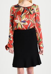 Röd långärmad blus med ett flerfärgat lövmönster och en svart kjol med utsvängd fåll. Blusen har en rund halsringning.