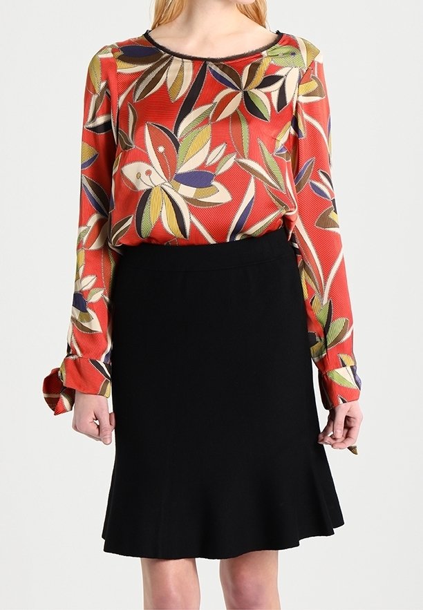 Röd långärmad blus med ett flerfärgat lövmönster och en svart kjol med utsvängd fåll. Blusen har en rund halsringning.