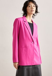 Fuchsia tailored blazer with notch lapels, single button closure, and two front pockets, paired with a black top and leather skirt.