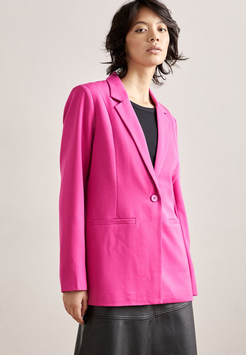 Fuchsia tailored blazer with notch lapels, single button closure, and two front pockets, paired with a black top and leather skirt.