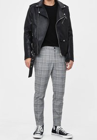 Černá kožená motocyklová bunda, žebrovaný černý svetr, šedé kárované kalhoty s modrými akcenty a černé tenisky.