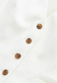 Gros plan d’un tissu blanc avec quatre boutons marron marbrés cousus en ligne verticale pour la fermeture.