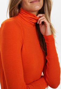 Pull col roulé orange côtelé avec manches longues et tissu doux et texturé. Le col est plié pour un détail supplémentaire.