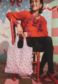 Újrahasználható szövet szatyor piros és fehér virágmintával, szív alakú motívumokkal és zöld növényekkel. Rövid fogantyúk, könnyű anyag és tágas.