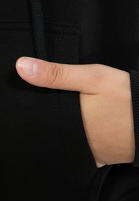 Felpa nera con tasca frontale, che mostra una mano con il pollice appoggiato all'interno della tasca. Il materiale sembra morbido e texturizzato.