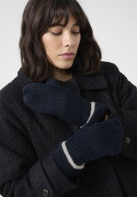 Marineblaue gestrickte Handschuhe aus strukturiertem Material mit einem kontrastierenden weißen Bündchen, getragen von einer Person in einem dunklen, strukturierten Mantel.