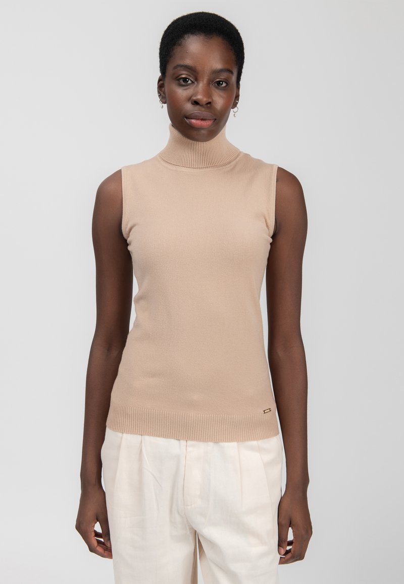 Maglione senza maniche color beige con colletto a dolce vita, orlo a costine, texture morbida, design minimale, abbinato a pantaloni color crema, dettaglio del logo oro sottile.