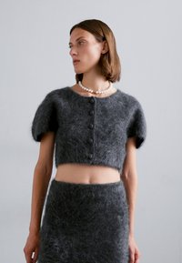 Cropped top grigio peloso con maniche corte, caratterizzato da un collo rotondo e cinque bottoni sulla parte anteriore, abbinato a una gonna grigia coordinata.