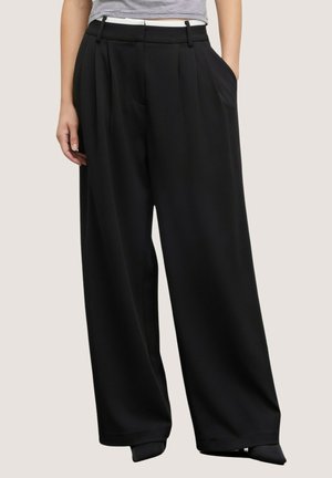 Kobieta ubrana w czarne, wysokowalne spodnie z szerokimi nogawkami, z zakładkami i bocznymi kieszeniami, w połączeniu z krótkim, pasiastym topem z krótkim rękawem.