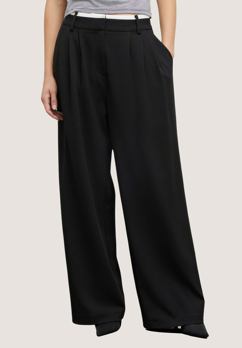 Femme portant un pantalon noir taille haute à jambes larges avec des plis et des poches latérales, associé à un crop top rayé à manches courtes.