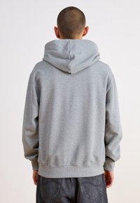 Grå huvtröja med avslappnad passform, ribbade ärmslut och nederkant, mjuk textur och en rymlig huva. Sedd från baksidan.