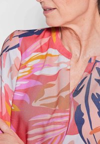 Blusa floreale in tessuto leggero, caratterizzata da motivi rosa, arancio e navy. Collo rotondo con vestibilità ampia e design astratti e colorati.
