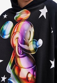 Sudadera con capucha negra que presenta un gráfico colorido y brillante de Mickey Mouse. El fondo tiene estrellas blancas, destacando el diseño vibrante y la textura general.