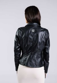Svart läderjacka med en figurnära design, med snittkrage och sidodetaljer med dragkedja. Har en märkespatch på baksidan. Strukturerad yta.