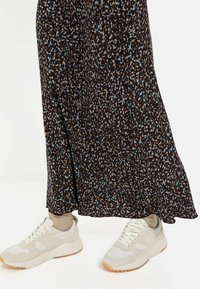 Hvide sneakers med beige accenter, parret med en mørk blomsterfarvet nederdel med blå og brune prikker, der går ned til anklerne.