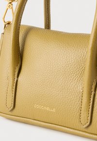 Mala de mão em pele verde-oliva com superfície texturizada, alças curtas e ferragens em tom dourado. Apresenta o nome da marca gravado em relevo.