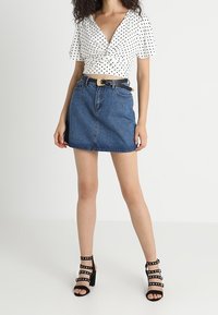 Bílý krátký rukáv top s černými puntíky, doplněný modrou džínovou mini sukní a černými sandály na podpatku s pásky a cvočky.