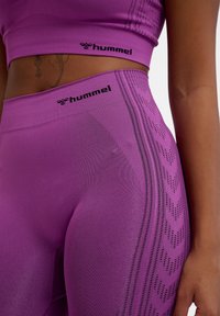 Paarse sportoutfit met een cropped top en high-waisted leggings. Gestructureerde stof met patroonaccenten en logo-details.