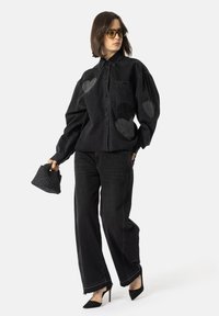 Svart denimskjorte med hjerteformede lapper, parret med svarte vide jeans og svarte høye hæler. Tilbehøret inkluderer en vevd håndveske.