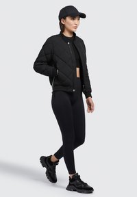 Zwarte gewatteerde bomberjack met een ronde kraag, gecombineerd met een zwarte crop top en hoge taille legging, afgewerkt met zwarte gestructureerde sneakers.