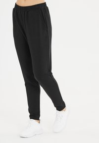 Zwarte sweatpants met een elastische tailleband, twee zijzakken en taps toelopende benen. Gepaarde met witte sport schoenen voor contrast.