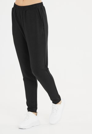 Black sweatpants with an elastic waistband, two side pockets, and tapered legs. Paired with white athletic shoes for contrast.