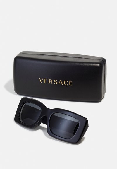 Mustad ülemõõdulised päikeseprillid tumedate läätsedega ja paksu ruudukujulise raamiga. Kaasas mattmust karp, millel on kuldne "VERSACE" kiri.