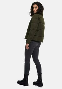 Dark green puffer jacket with a high collar and horizontal seams, paired with black skinny jeans and ankle boots.