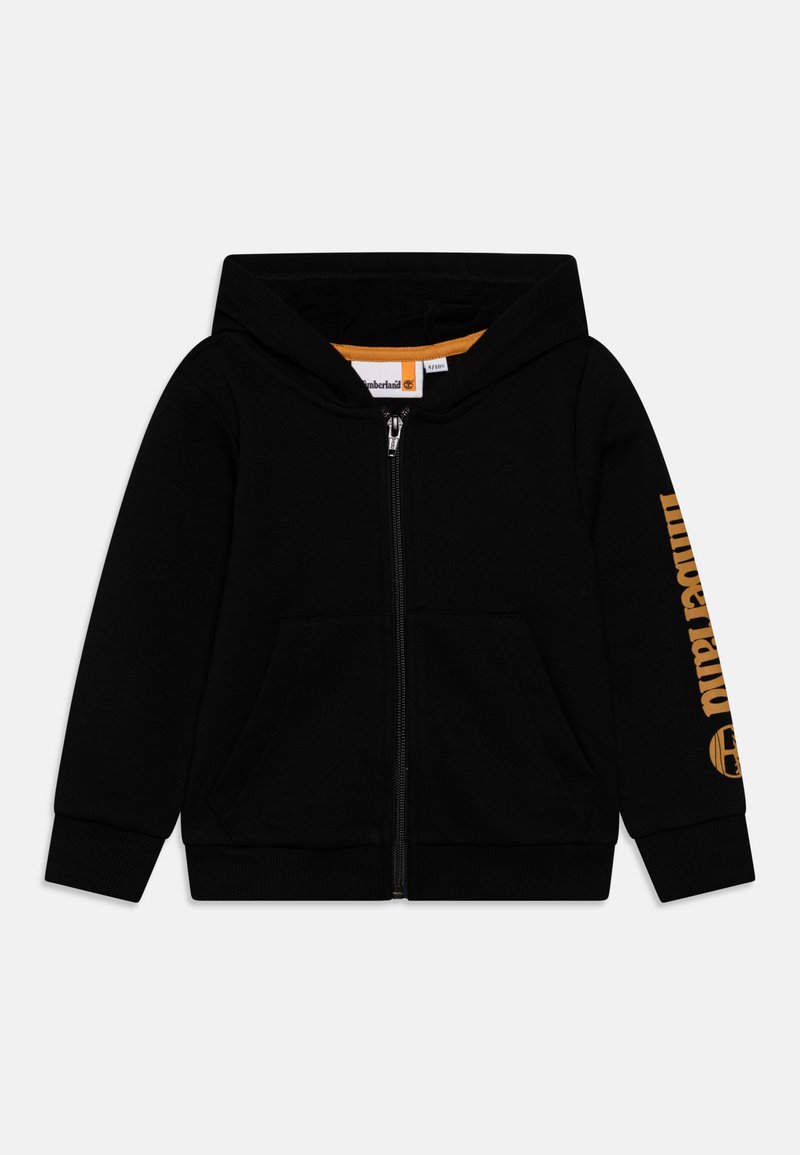 Hoodie noir zippé en tissu doux, avec une doublure intérieure orange, des poches avant et un logo sur la manche gauche.