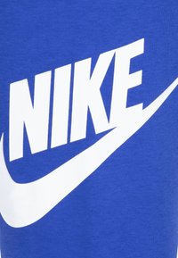Modra bombažna majica z velikim belim logotipom "NIKE" in obliko prečke, z gladko teksturo in brez dodatnih vzorcev ali akcentov.