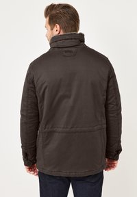 Schwarze isolierte Jacke mit hohem Kragen, texturiertem Stoff und knöpfbaren Manschetten; eine nahtdetails sorgen für Struktur im Design.