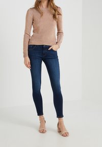 Ljust rosa, långärmad, strukturerad tröja i kombination med mörkblå, slim fit-jeans och beige, kraftiga klacksandaler.