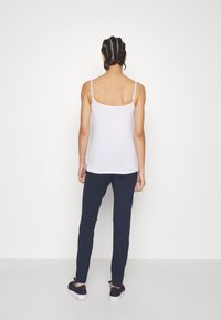 Débardeur blanc à bretelles spaghetti avec une coupe ajustée, associé à un pantalon bleu marine foncé et des chaussures noires. Texture lisse, style minimaliste.