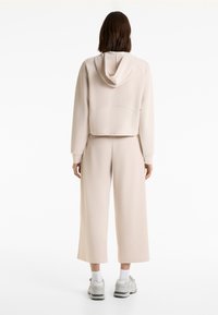 Beige hoodie met ribbeltextuur, cropped ontwerp, gecombineerd met wijde broekspijpen. Draagt witte sokken en lichtgrijze sneakers.