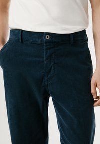Los pantalones de pana en color navy presentan un corte recto, una textura acanalada, bolsillos frontales y un cierre de botón metálico en la cintura.