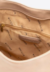 Interno di una borsa di colore beige chiaro con una tasca con cerniera, texture morbida e logo "WITTCHEN" impresso sulla fodera in tessuto.