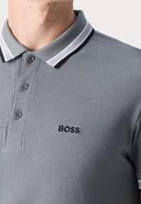 T-shirt polo gris en tissu texturé, doté d'un col côtelé avec des accents blancs et noirs, de trois boutons et d'un logo "BOSS".