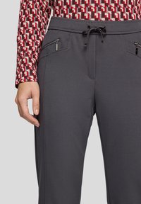 Grau gemusterte Hose mit Kordelzugbund. Mit Reißverschlusstaschen vorne und schmaler Passform, präsentiert mit einem gemusterten Langarmoberteil.