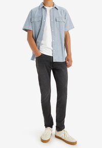 Randig kortärmad skjorta i blått och vitt, bärs över en vit t-shirt; kombineras med mörka jeans och sneakers i beige.